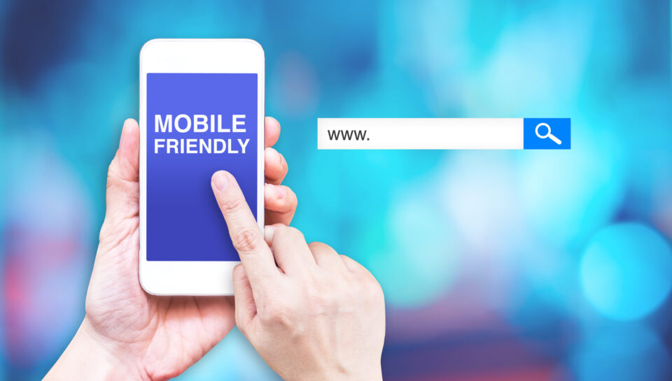 Hand touch mobile phone with  mobile friendly word with search box at blurred blue background, Digital marketing business concept.